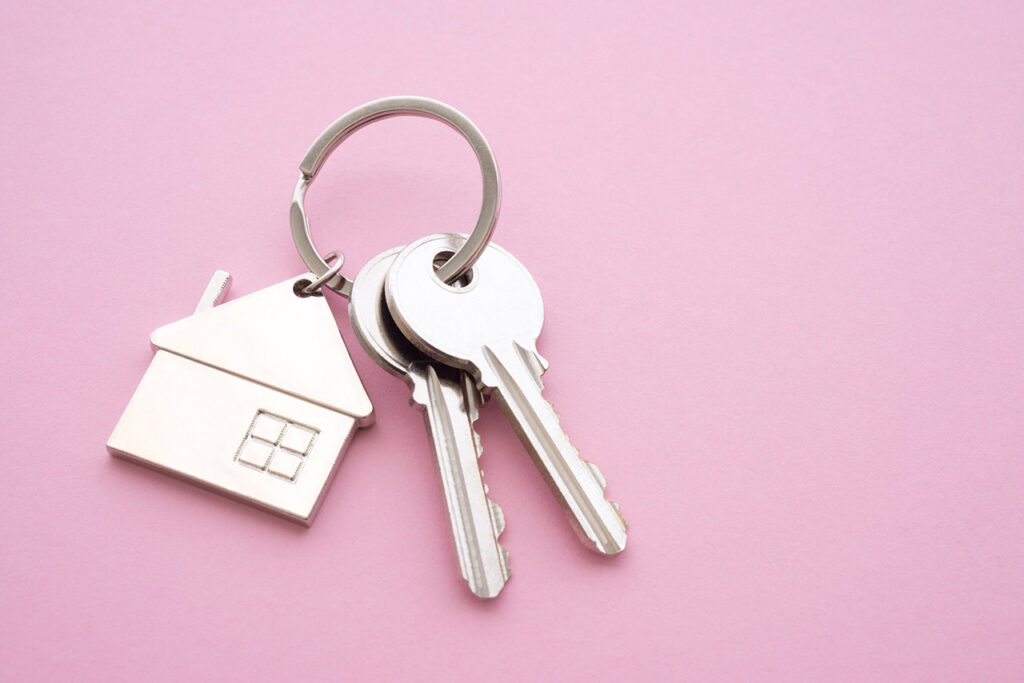 Silver house key with house keychain on pink background